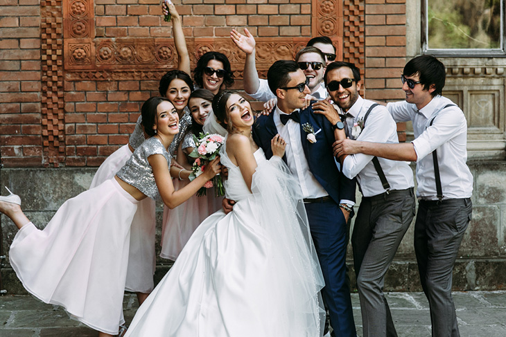 A bride and groom laugh and pose for a goofy photo with bridesmaids and groomsmen