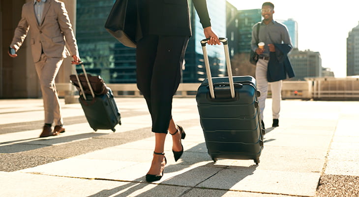 A group of travelers with luggage walk outside an airport