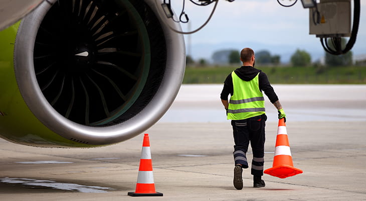 An airline employee walks with a traffic cone on an airplane tarmac 