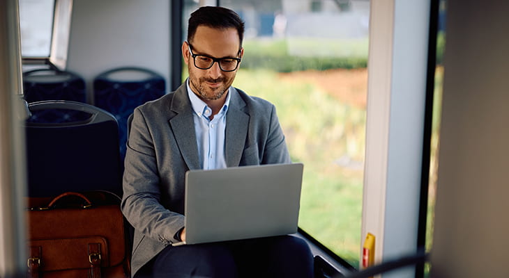 An employee types on a laptop while sitting in a bus cabin