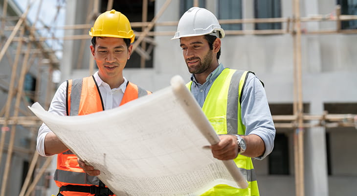 Two construction workers look over a blueprint at a work site